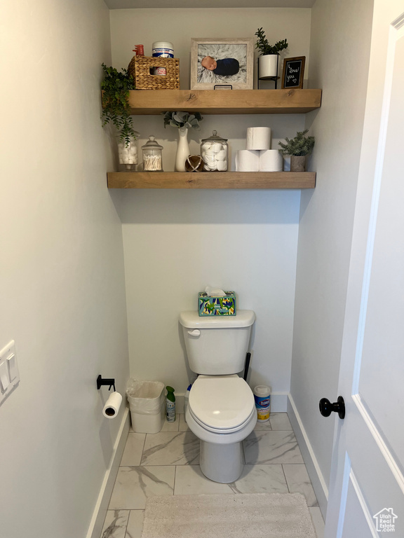 Bathroom with marble look tile flooring, toilet, and baseboards