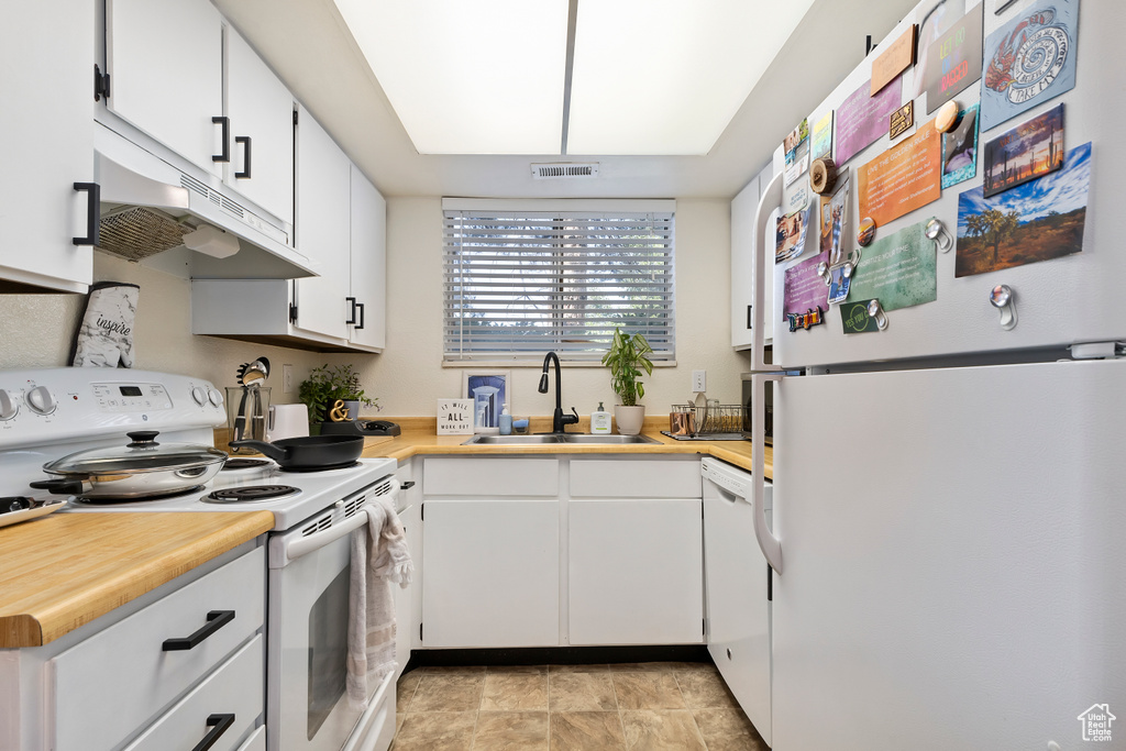 Kitchen featuring white appliances, a sink, light countertops, white cabinets, and under cabinet range hood