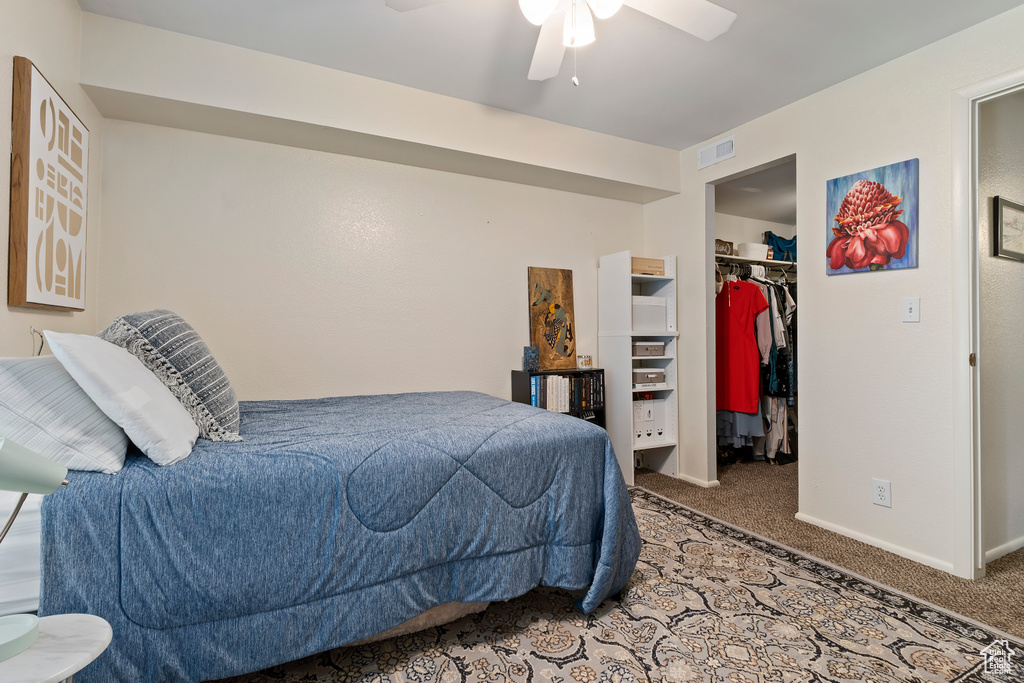 Carpeted bedroom with a spacious closet, a closet, baseboards, and a ceiling fan