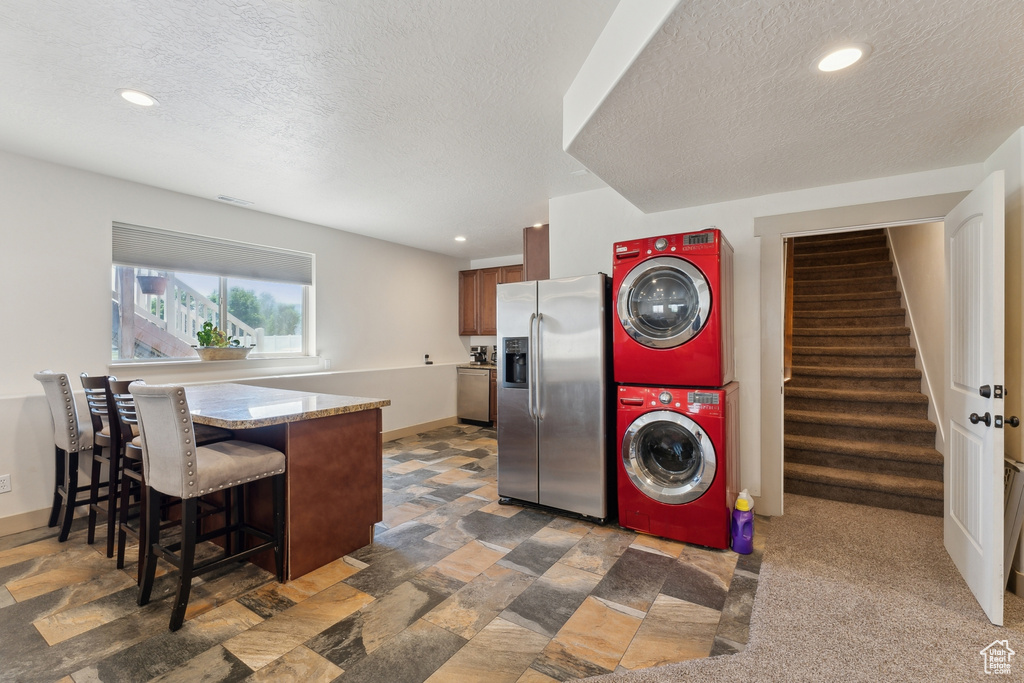 Kitchen featuring stainless steel refrigerator with ice dispenser, stacked washer / dryer, a breakfast bar, a textured ceiling, and a peninsula