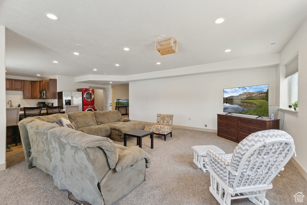 Living area with estacked washer and dryer, recessed lighting, light colored carpet, and baseboards