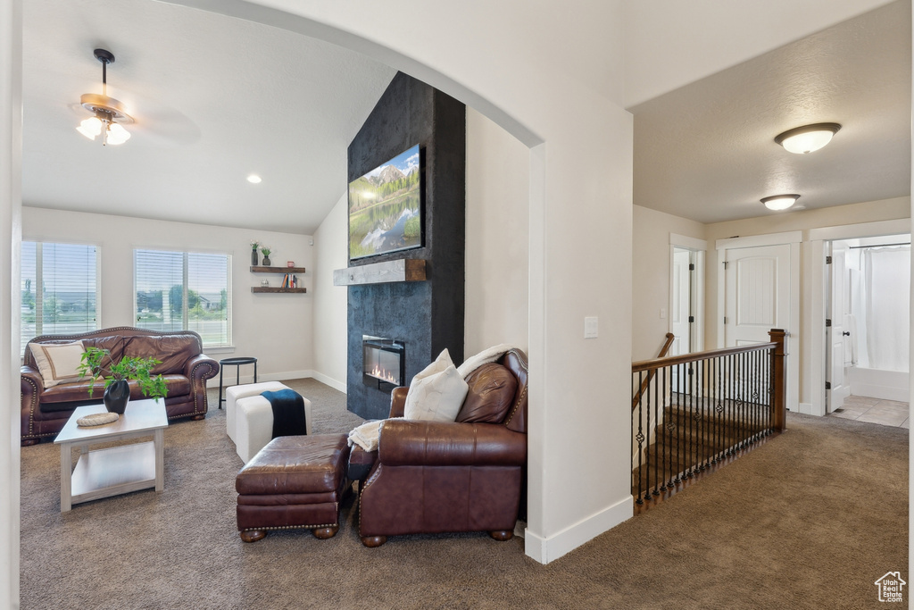 Carpeted living area with a fireplace, lofted ceiling, a ceiling fan, arched walkways, and baseboards