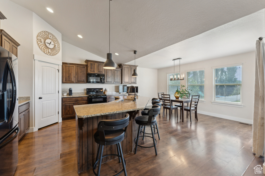 Kitchen with black appliances, a sink, recessed lighting, a kitchen bar, and dark wood-style floors