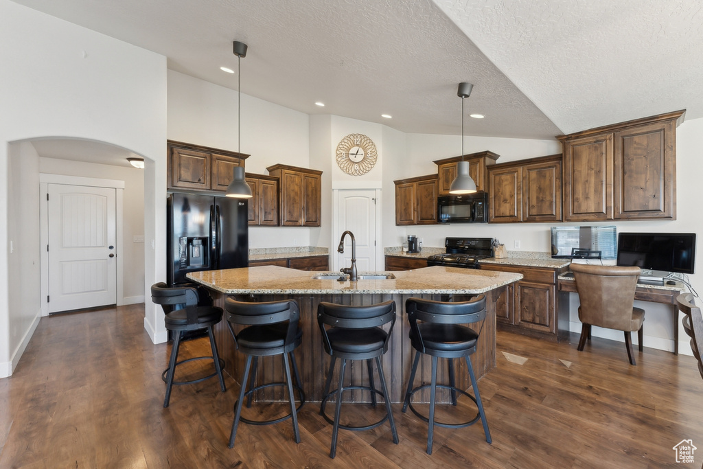 Kitchen featuring a sink, black appliances, an island with sink, light stone counters, and a kitchen bar