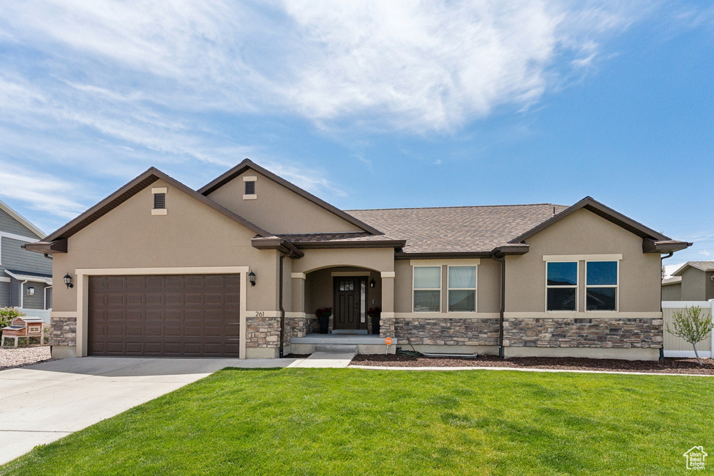 View of front facade featuring stucco siding, stone siding, driveway, an attached garage, and a front yard