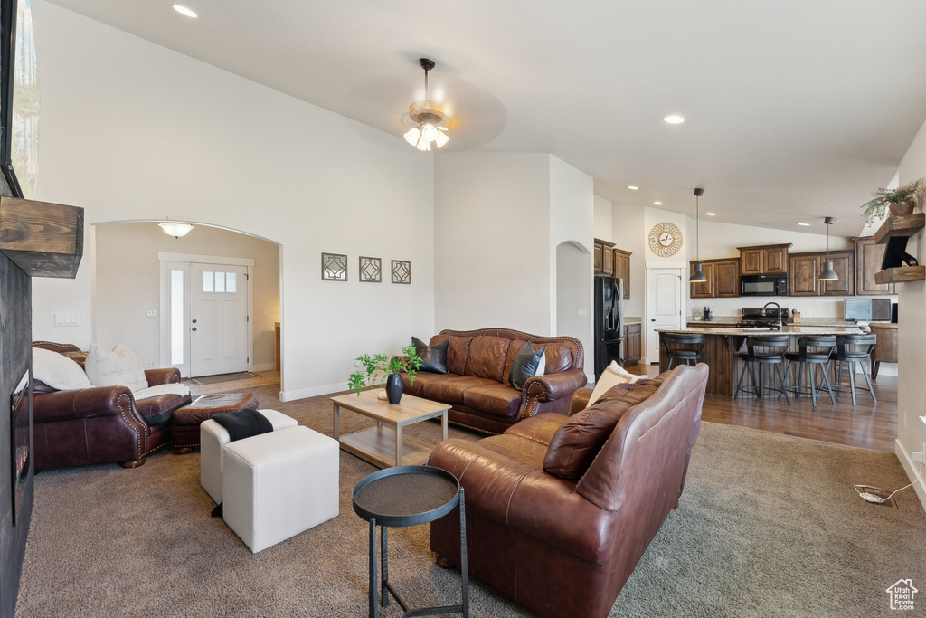 Carpeted living area with a sink, arched walkways, recessed lighting, high vaulted ceiling, and baseboards
