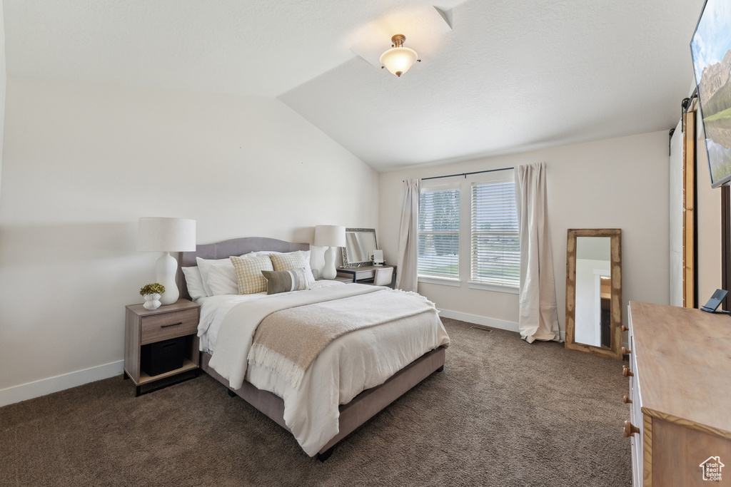 Bedroom with lofted ceiling, dark carpet, and baseboards