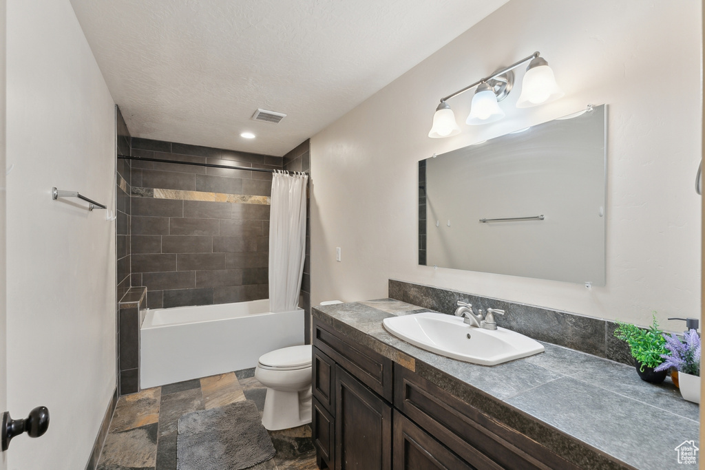 Bathroom featuring vanity, toilet, stone finish flooring, and shower / bathtub combination with curtain