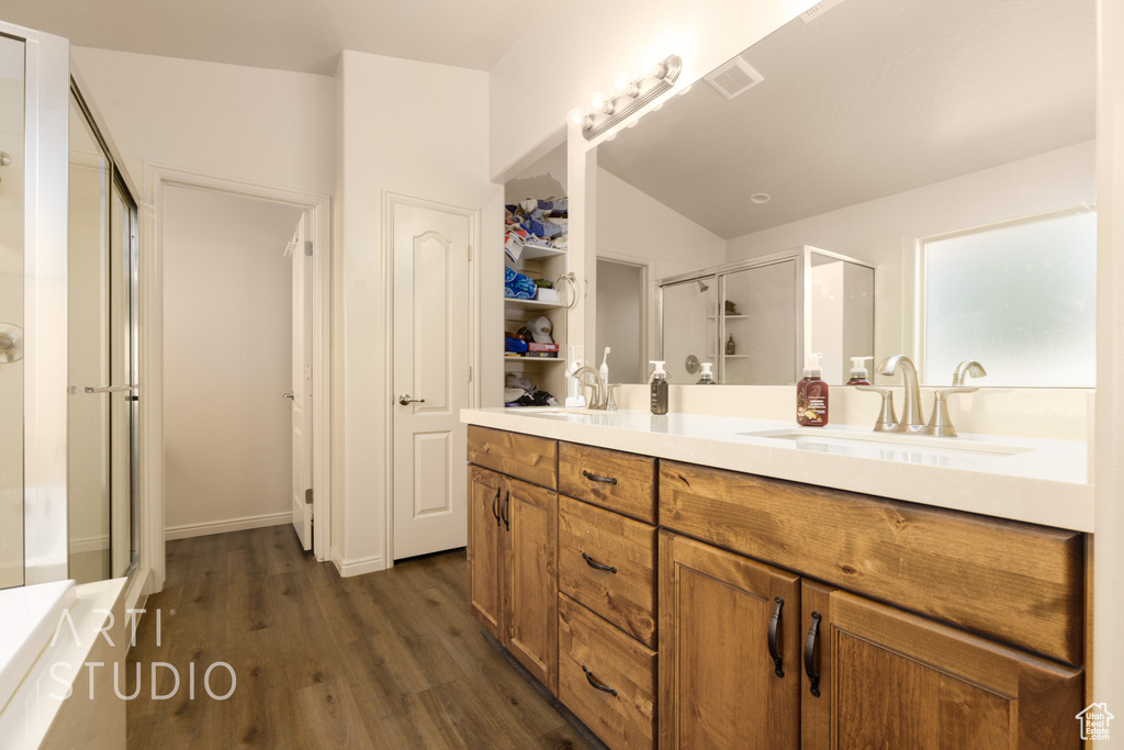 Full bathroom featuring a shower stall, double vanity, wood finished floors, a bath, and lofted ceiling