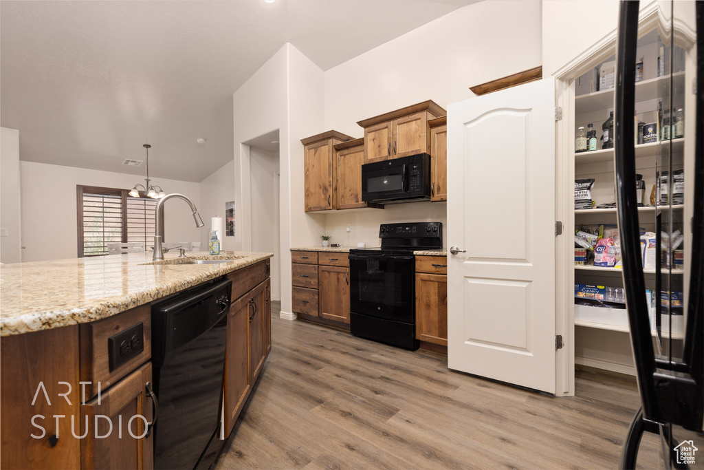 Kitchen featuring black appliances, a sink, light wood-style flooring, light stone counters, and lofted ceiling