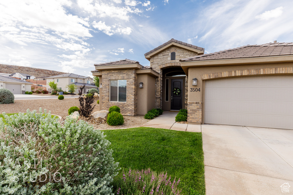 View of front facade featuring concrete driveway, stucco siding, a garage, stone siding, and a tile roof