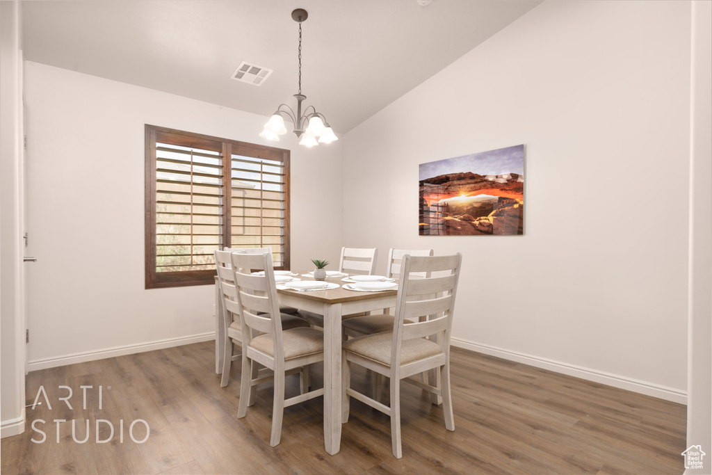 Dining room featuring wood finished floors, vaulted ceiling, baseboards, and a chandelier