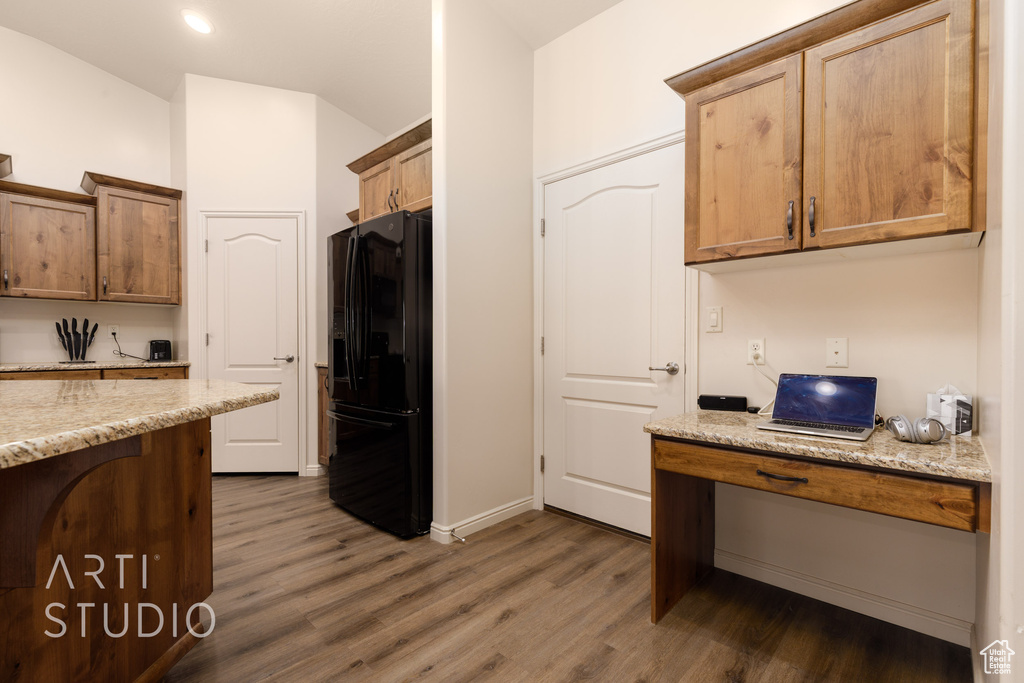 Kitchen with black fridge with ice dispenser, dark wood-type flooring, light stone countertops, lofted ceiling, and baseboards