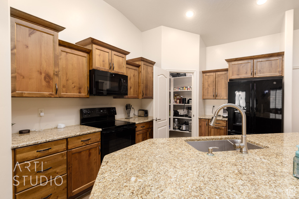 Kitchen with black appliances, a sink, light stone counters, vaulted ceiling, and brown cabinets
