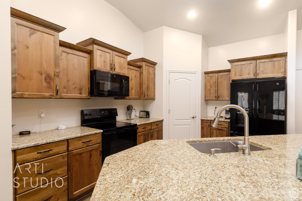 Kitchen featuring black appliances, a sink, lofted ceiling, brown cabinets, and light stone countertops
