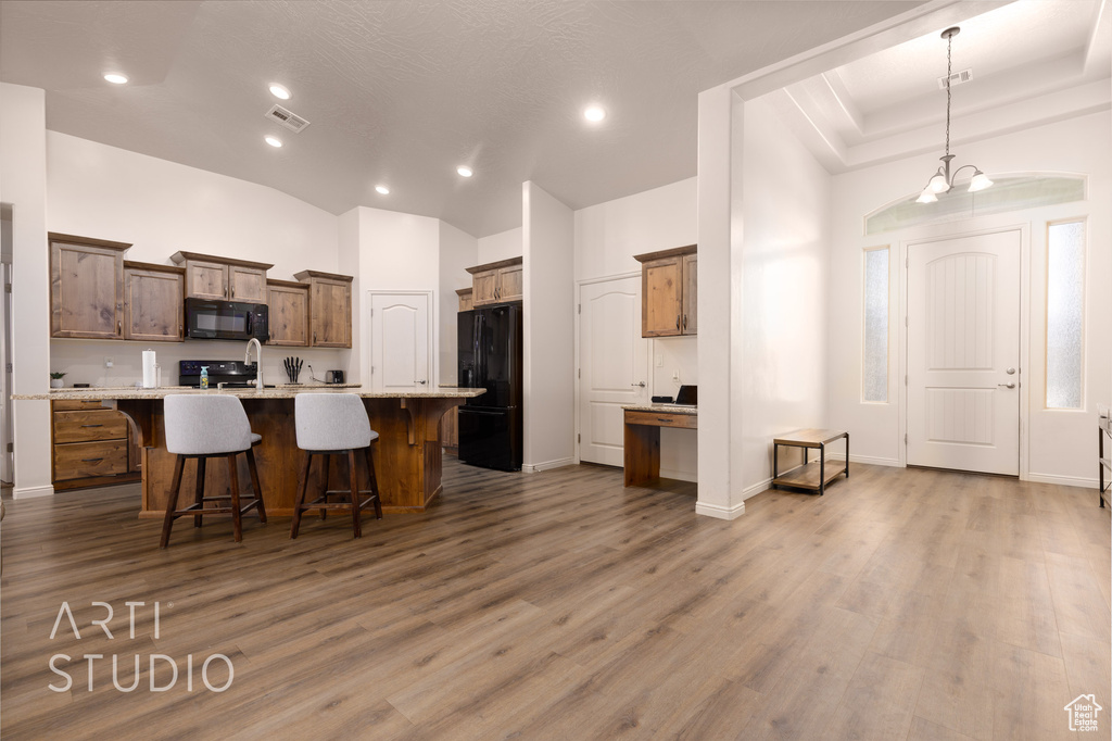 Kitchen featuring black appliances, a kitchen bar, wood finished floors, a center island with sink, and recessed lighting