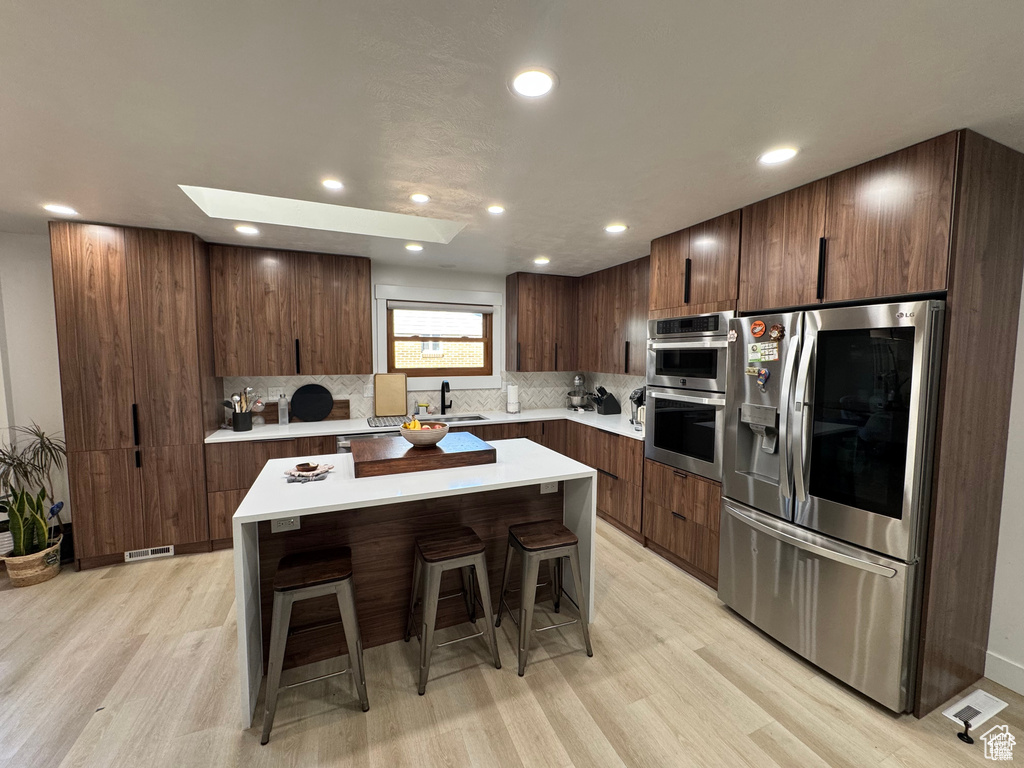 Kitchen featuring appliances with stainless steel finishes, a kitchen breakfast bar, a sink, modern cabinets, and light countertops