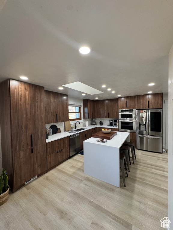Kitchen with appliances with stainless steel finishes, light wood-style flooring, recessed lighting, a sink, and light countertops