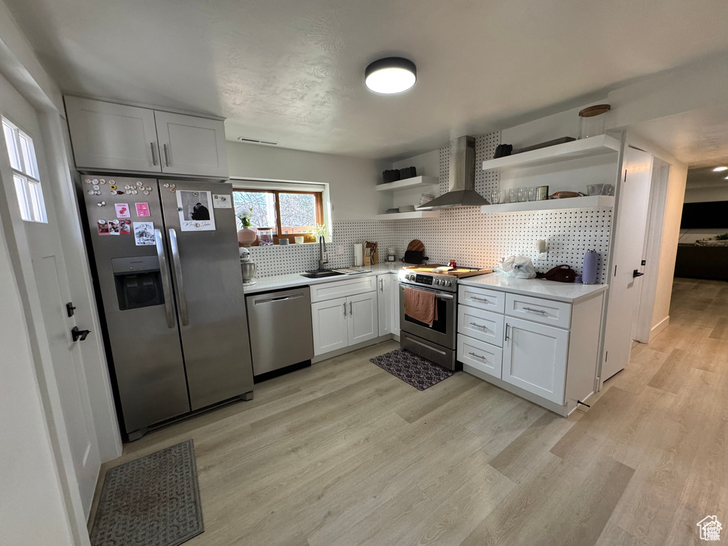 Kitchen featuring appliances with stainless steel finishes, open shelves, wall chimney exhaust hood, backsplash, and a sink