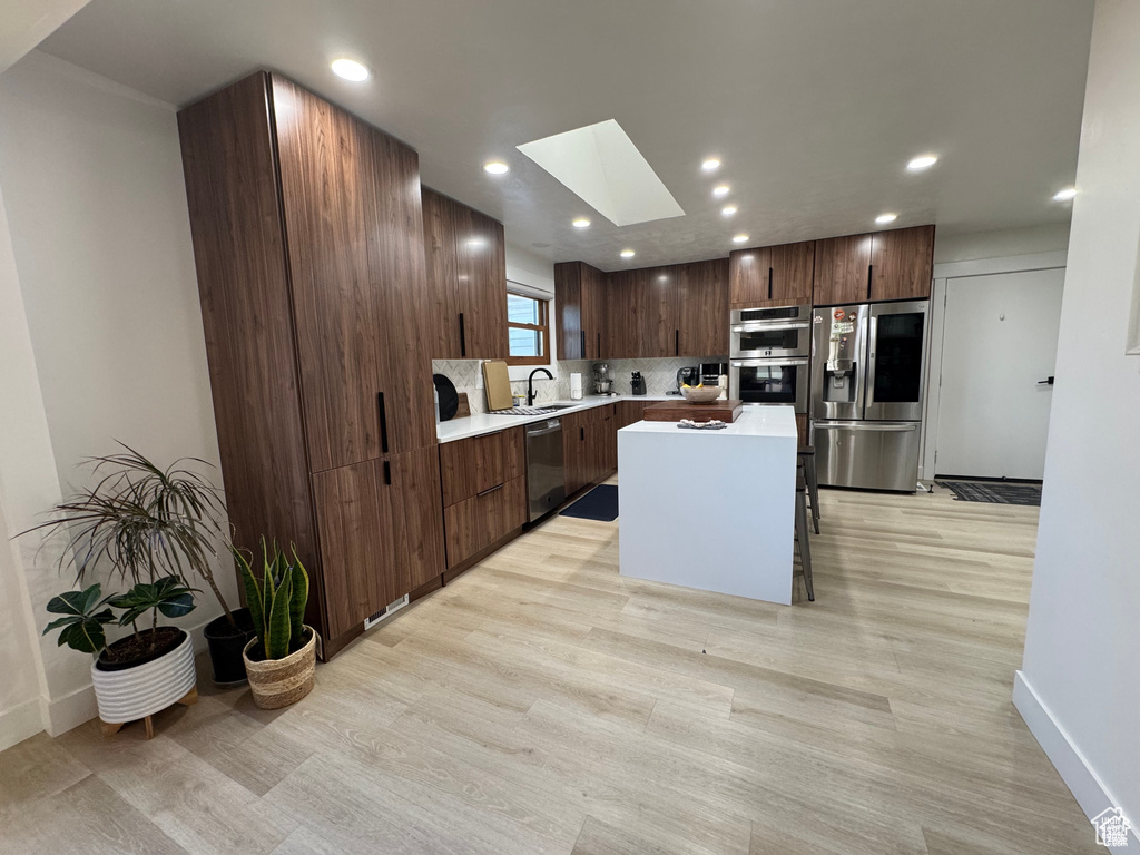 Kitchen with stainless steel appliances, a skylight, light countertops, light wood finished floors, and recessed lighting