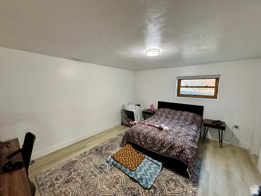 Bedroom with light wood-type flooring, baseboards, and a textured ceiling
