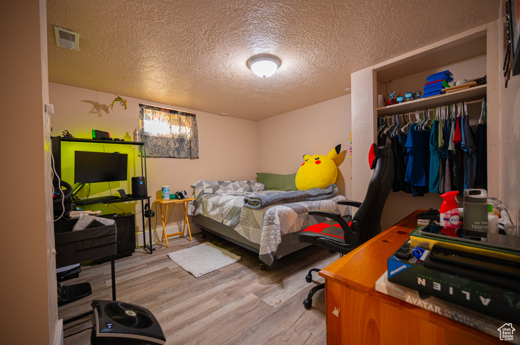 Bedroom with wood finished floors, a textured ceiling, and a closet