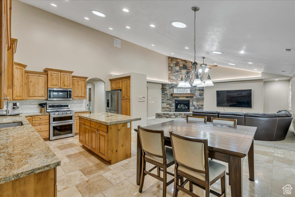 Kitchen with appliances with stainless steel finishes, a stone fireplace, recessed lighting, open floor plan, and decorative backsplash