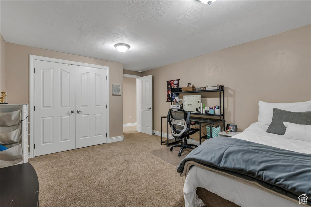 Bedroom featuring light carpet, baseboards, a closet, and a textured ceiling
