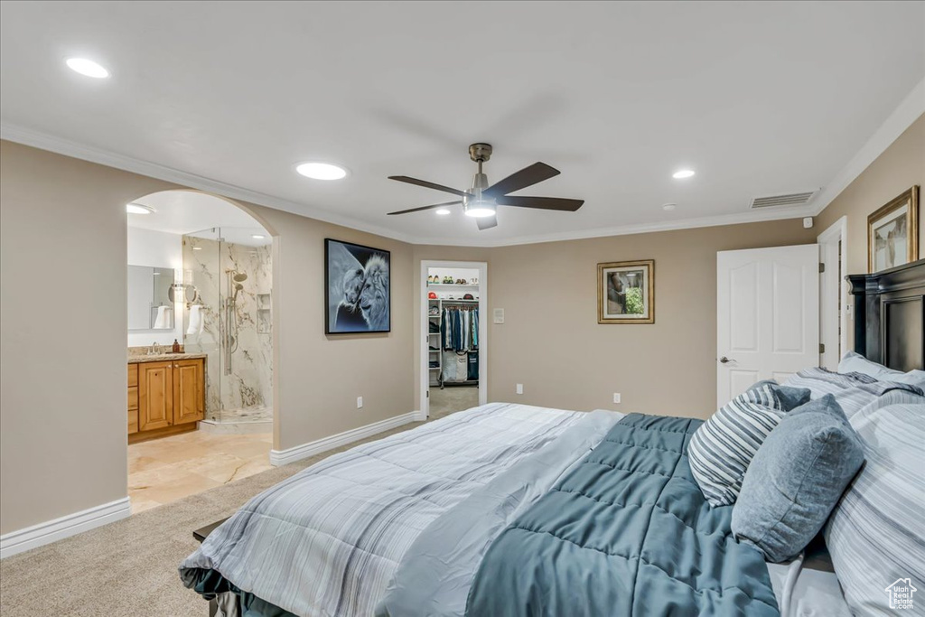Bedroom with recessed lighting, crown molding, arched walkways, a walk in closet, and light carpet