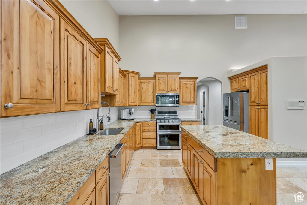 Kitchen featuring stainless steel appliances, a sink, a kitchen island, a towering ceiling, and decorative backsplash