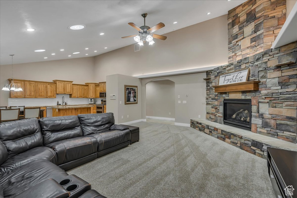 Living area with a stone fireplace, a ceiling fan, high vaulted ceiling, light carpet, and recessed lighting