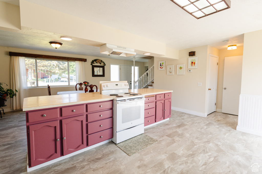 Kitchen with electric stove, red cabinets, under cabinet range hood, and light countertops