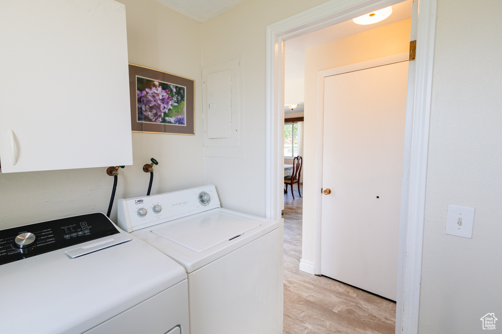 Laundry room with light wood-type flooring, washer and clothes dryer, and electric panel