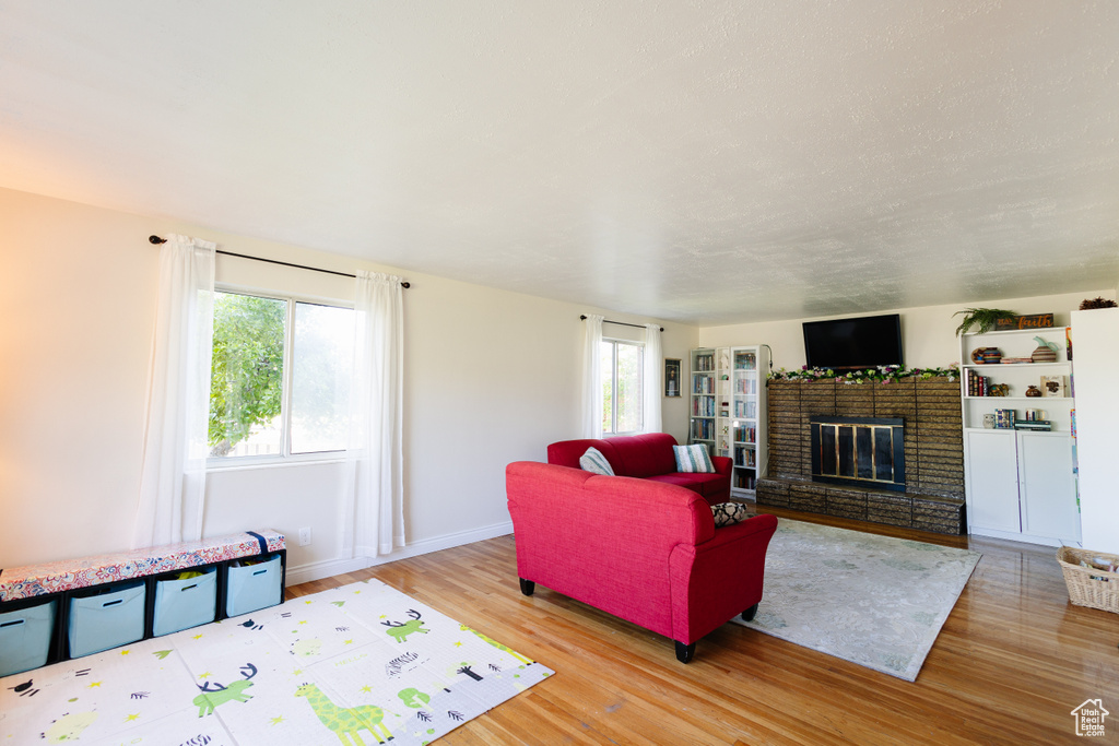 Living room with wood finished floors, a brick fireplace, healthy amount of natural light, and baseboards