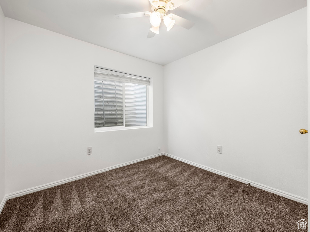 Empty room with dark carpet, ceiling fan, and baseboards