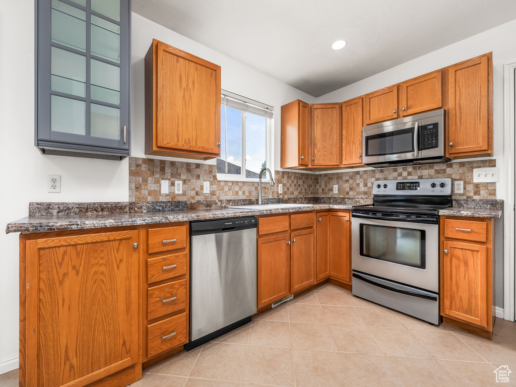 Kitchen with appliances with stainless steel finishes, a sink, brown cabinetry, and decorative backsplash