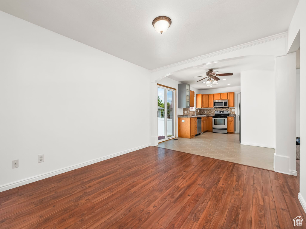 Unfurnished living room featuring ceiling fan, wood finished floors, a sink, and baseboards
