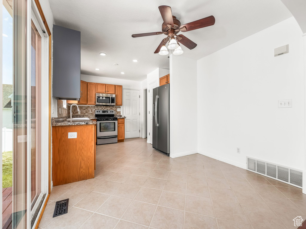 Kitchen with stainless steel appliances, a sink, backsplash, brown cabinetry, and ceiling fan