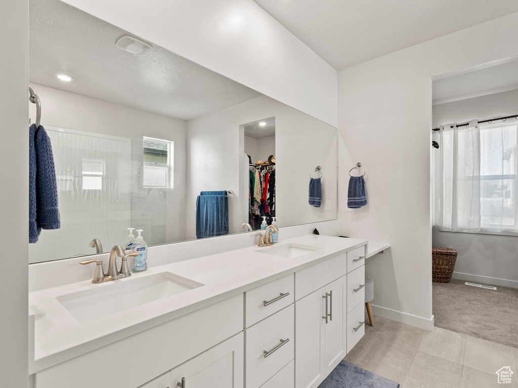 Full bathroom with double vanity, baseboards, a spacious closet, and a walk in shower