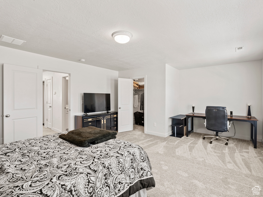 Bedroom with light carpet, baseboards, a spacious closet, a textured ceiling, and a desk