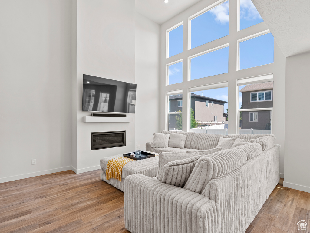 Living area with plenty of natural light, baseboards, wood-type flooring, a high ceiling, and a glass covered fireplace