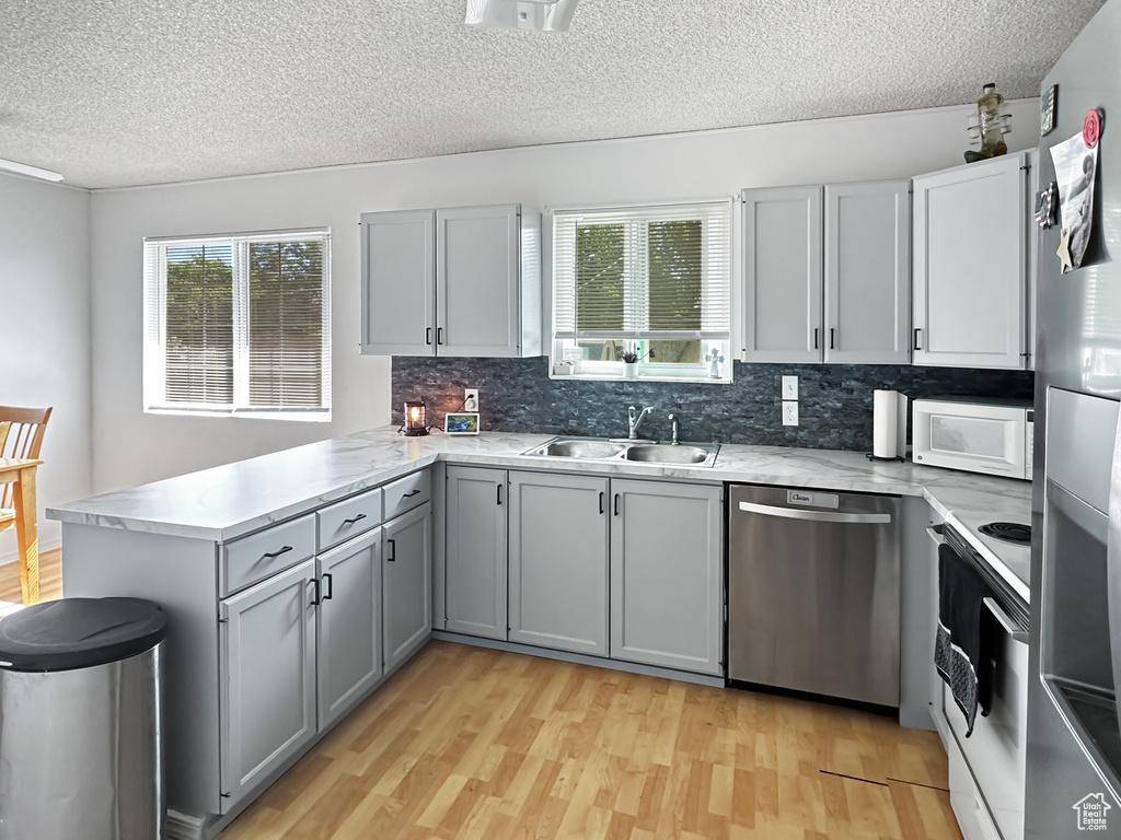 Kitchen featuring white appliances, a sink, a peninsula, plenty of natural light, and a textured ceiling
