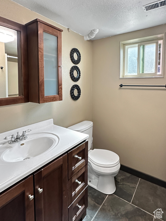 Bathroom featuring toilet, a textured ceiling, vanity, and tile patterned floors