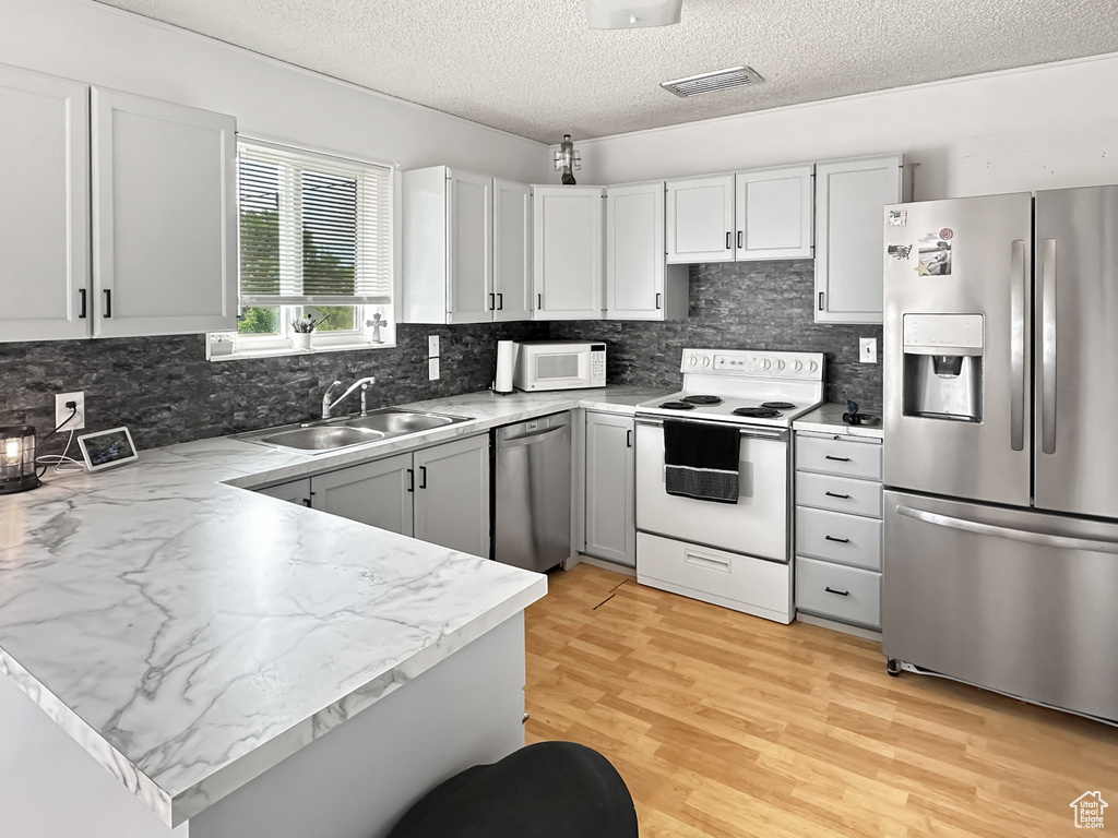 Kitchen featuring stainless steel appliances, a sink, a textured ceiling, tasteful backsplash, and light wood finished floors