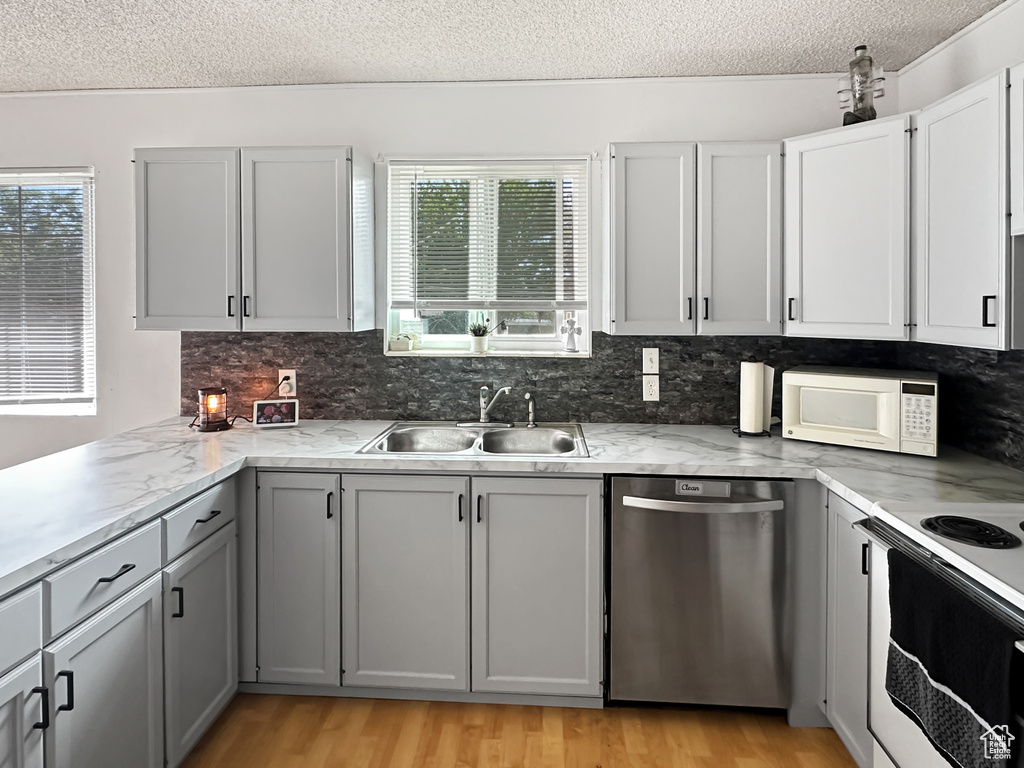 Kitchen featuring white appliances, a sink, a textured ceiling, gray cabinets, and tasteful backsplash