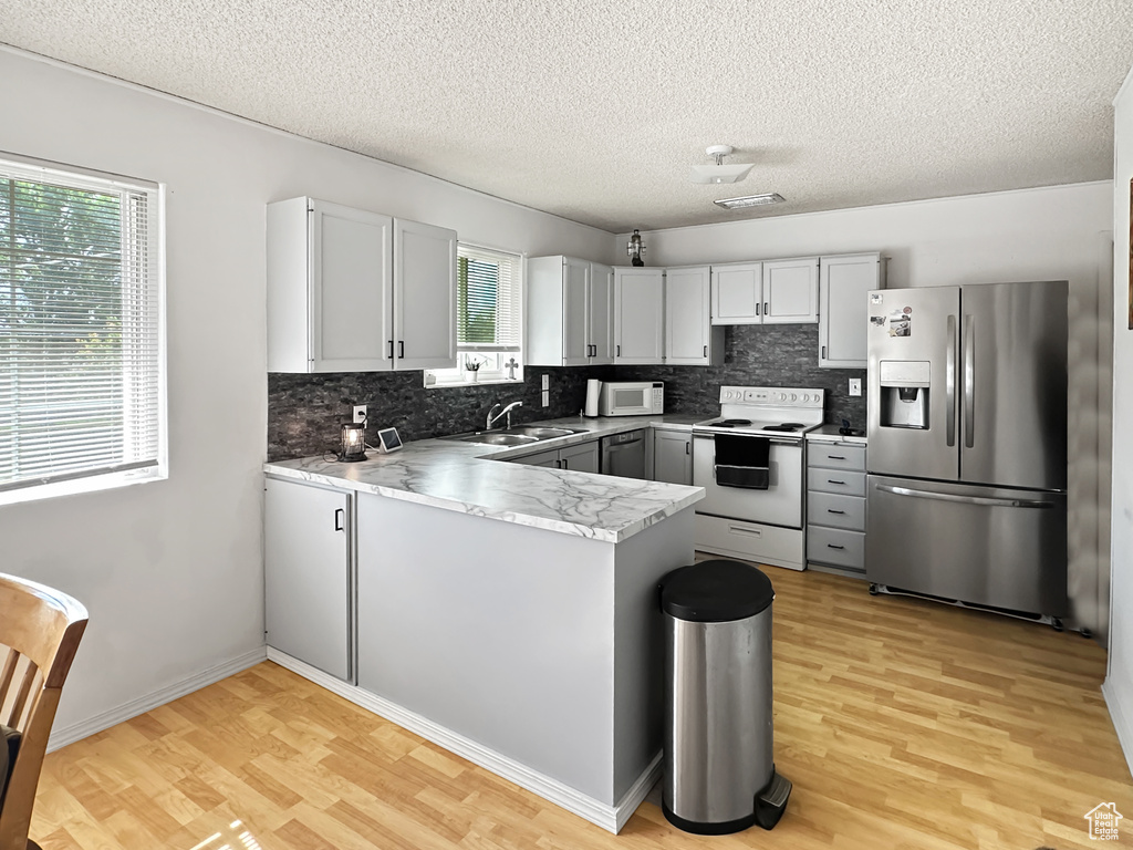 Kitchen featuring white appliances, light wood-type flooring, a sink, decorative backsplash, and a textured ceiling