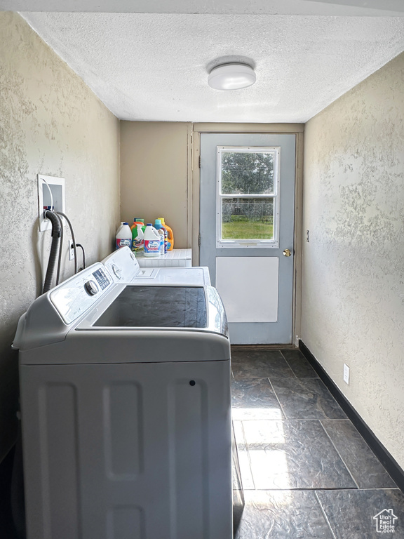 Laundry area with a textured wall, washing machine and dryer, a textured ceiling, baseboards, and stone tile flooring