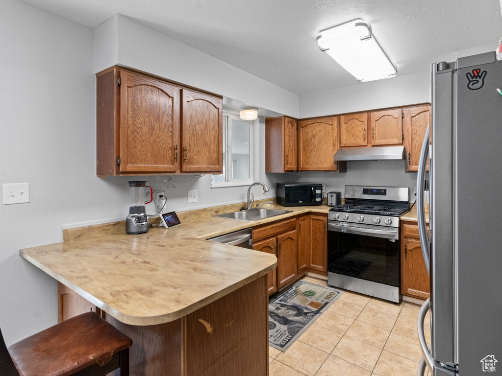 Kitchen featuring appliances with stainless steel finishes, a sink, a peninsula, under cabinet range hood, and brown cabinetry