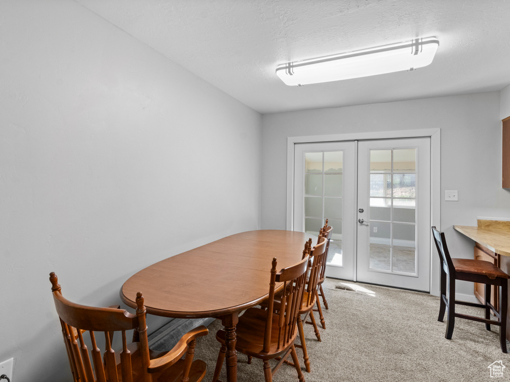 Carpeted dining area with french doors and a textured ceiling