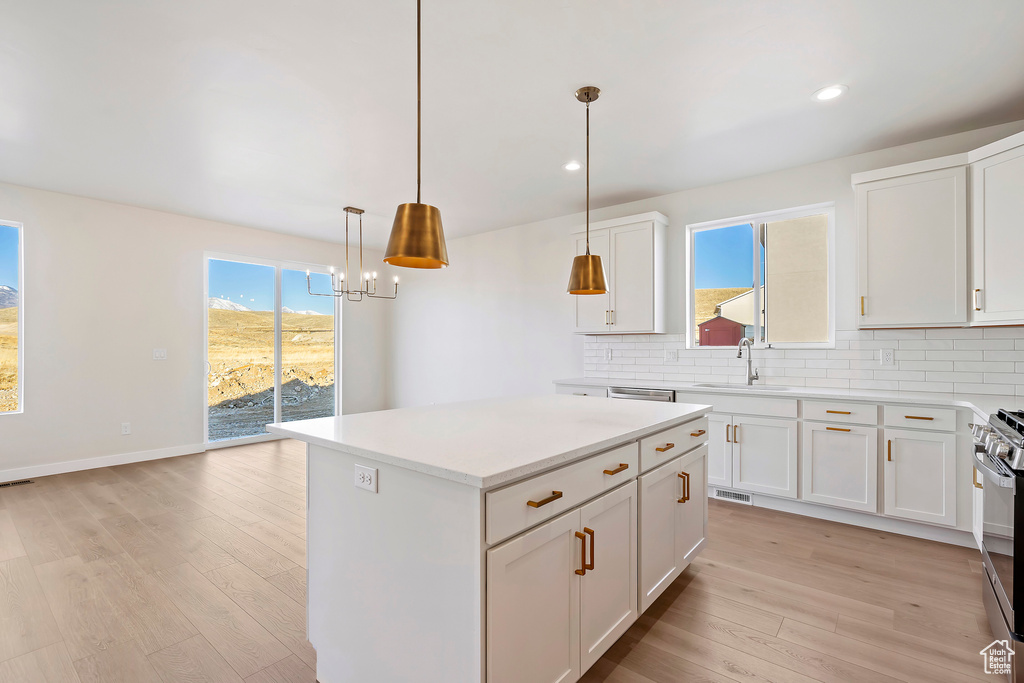 Kitchen with a sink, backsplash, light wood-style floors, white cabinets, and light countertops